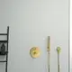 Thermostat von Ideal Standard in gebürstetem Gold, installiert an einer glatten Wand, mit einem Schlauch und Handbrause, daneben ein schwarzes Regal für Badezimmerutensilien.